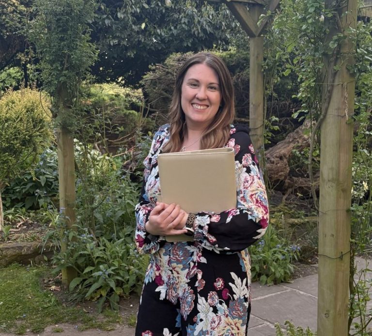 Owner and founder Molly holding a celebrant folder during a ceremony in Chester, standing in the garden.