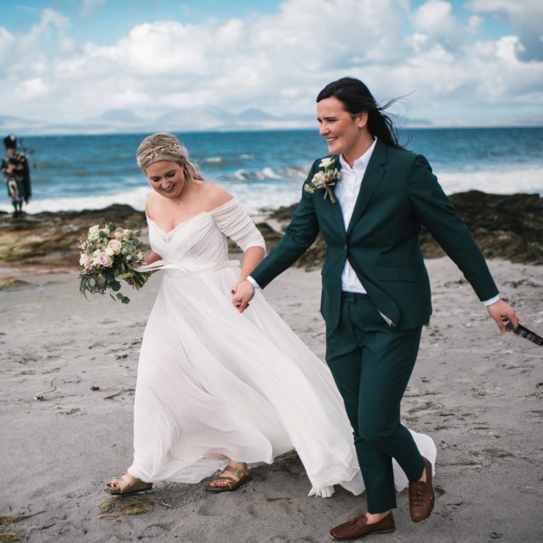 Same-sex couple walking hand in hand by the sea after their elopement with Molly’s Ceremonies