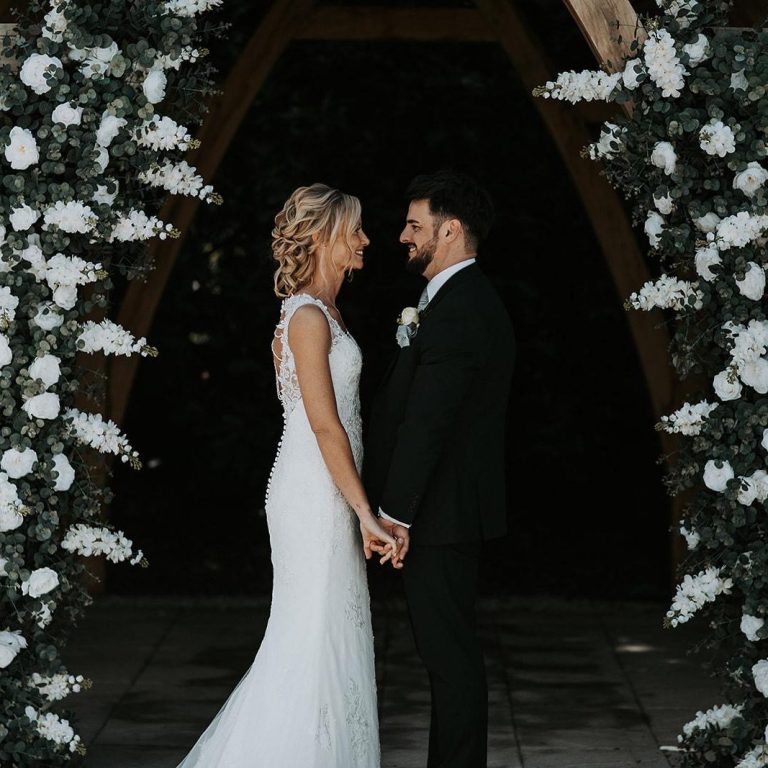 Happy couple holding hands under a floral archway during their wedding ceremony, officiated by Molly's Ceremonies.