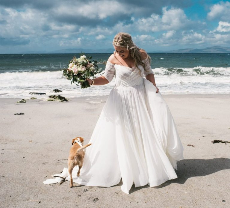 Bride holding flowers on the beach with her dog after an elopement ceremony by Molly’s Ceremonies