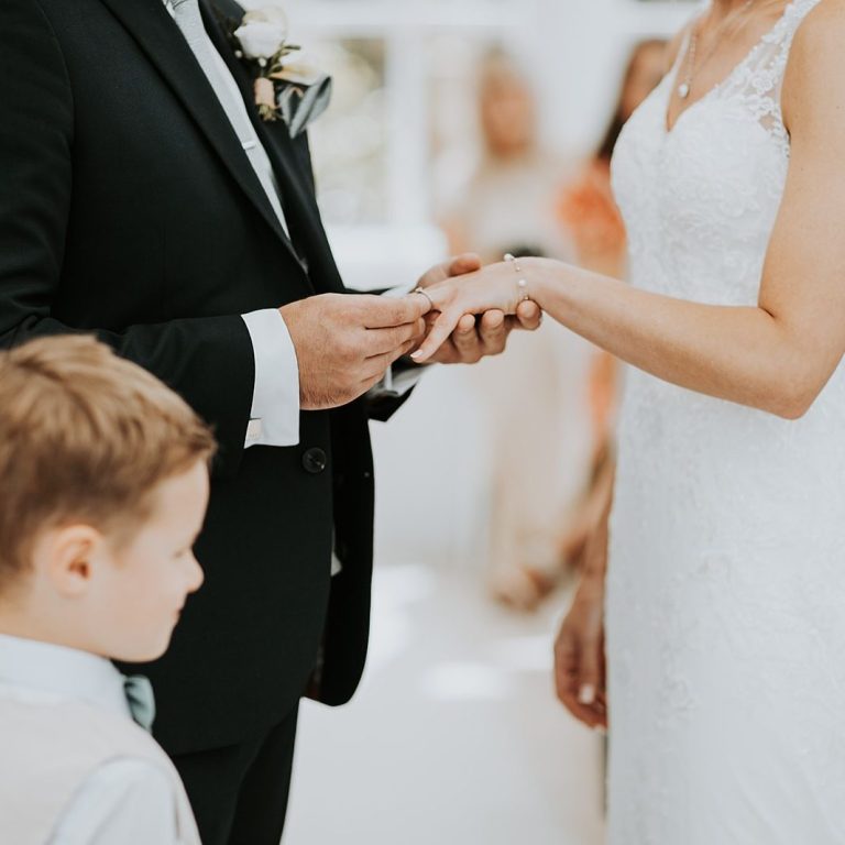 Close-up of the groom placing the wedding ring on the bride's finger while their child watches on.
