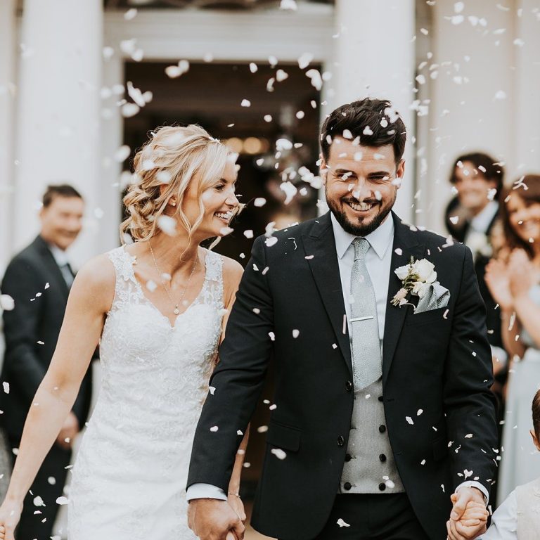 Bride and groom covered in confetti, with guests softly blurred in the background.