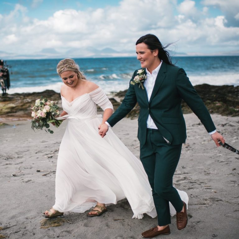 Same-sex couple walking hand in hand by the sea after their elopement with Molly’s Ceremonies
